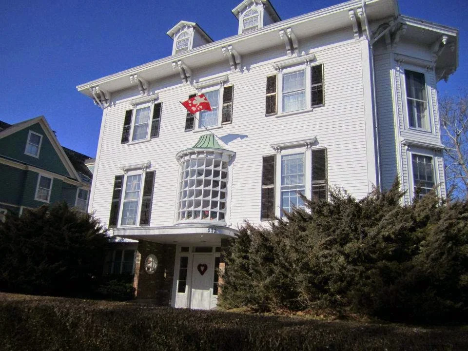 White Victorian house with mansard roof and red flower decoration on facade