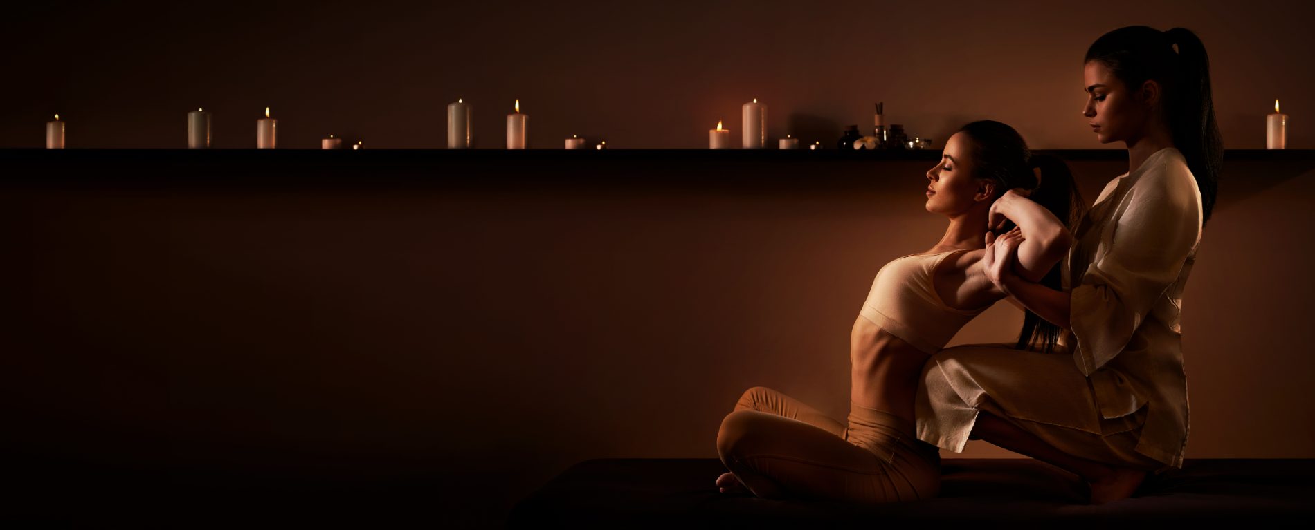Two women in spa setting with candlelit background during wellness treatment