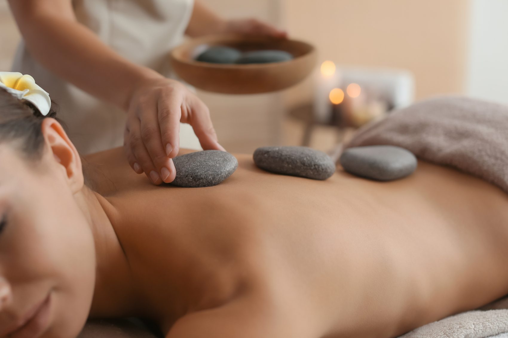 Spa therapist placing heated stones on client's back during massage treatment