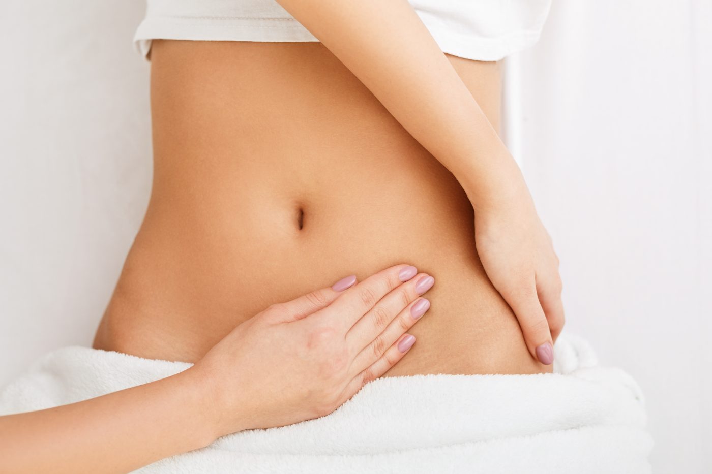 Woman receiving abdominal massage treatment on white towel