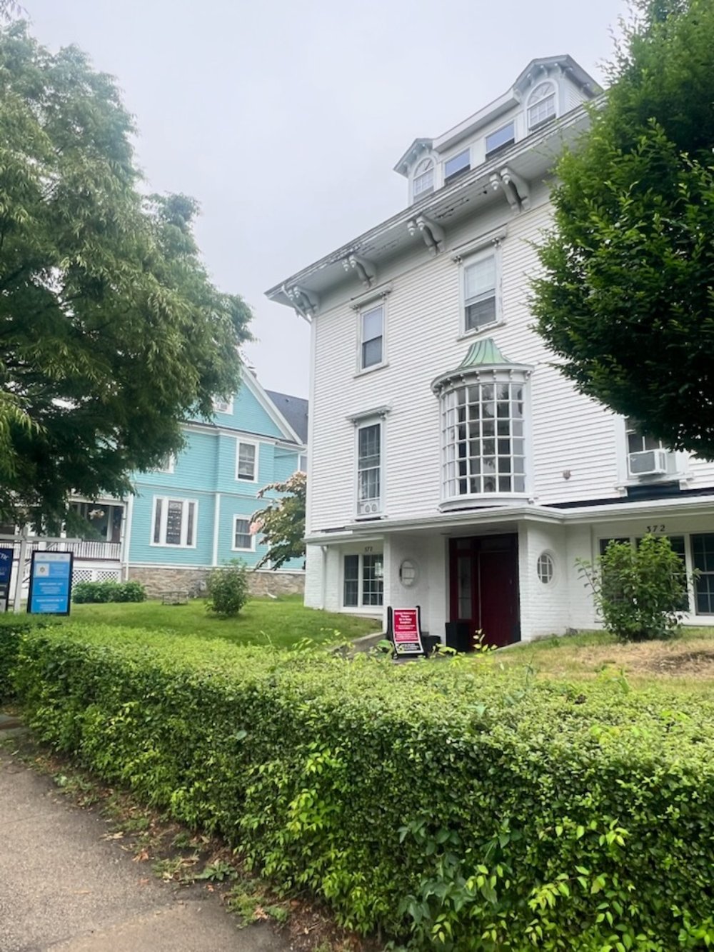 White Victorian house with turret and wraparound porch surrounded by green hedges
